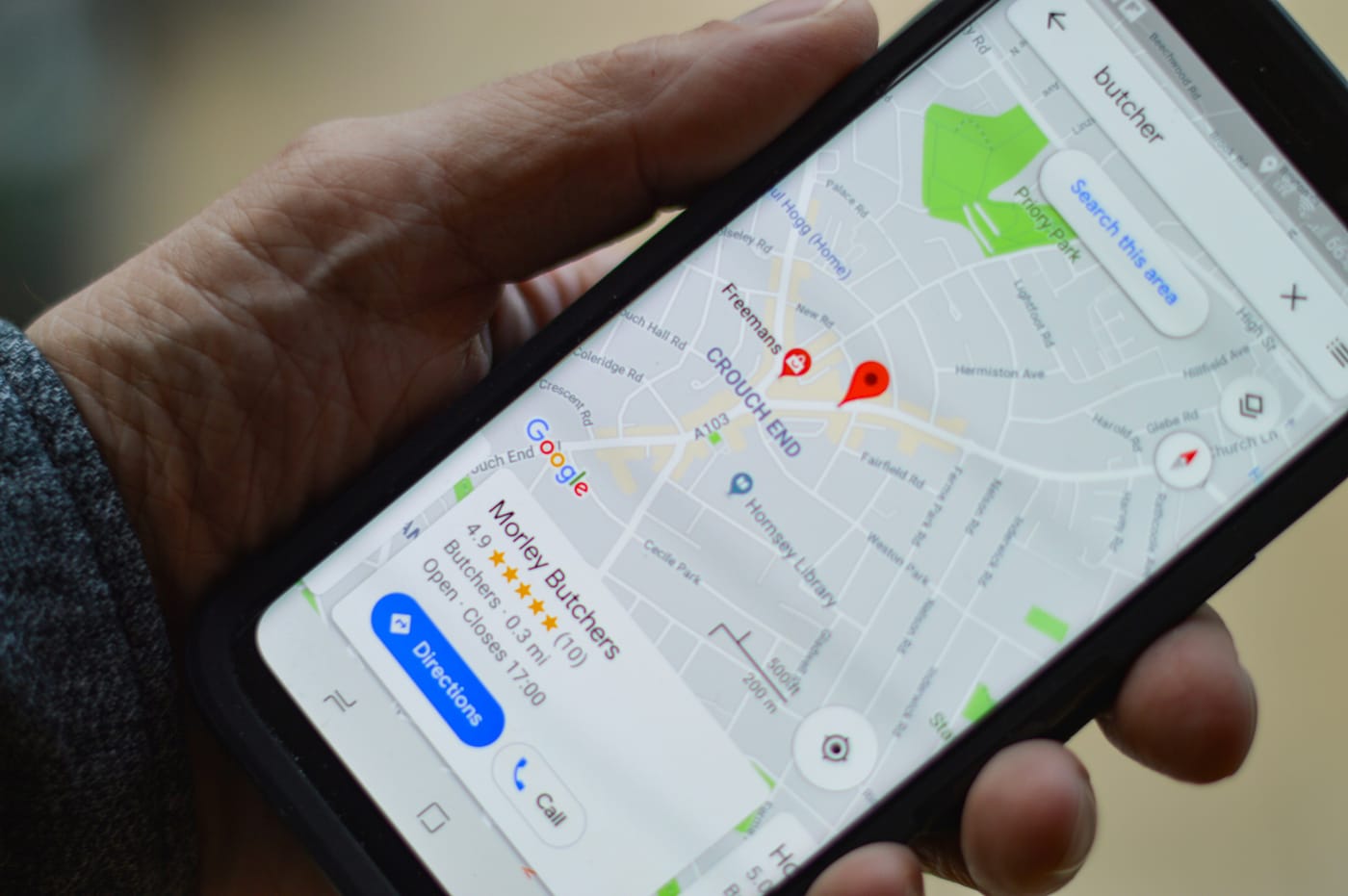Hand holding a phone showing a local map search with business listings