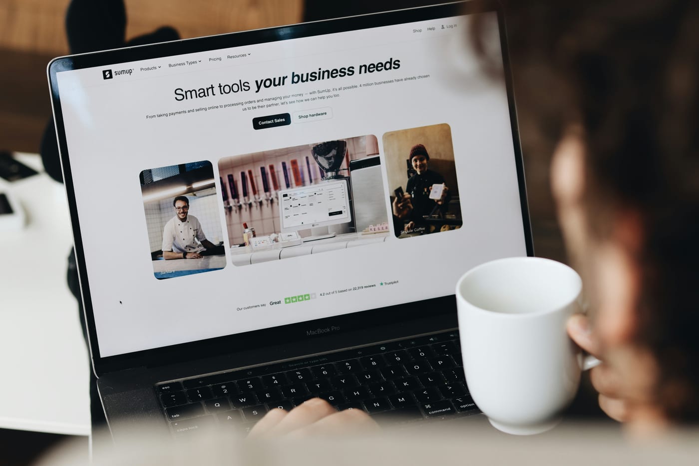 Person holding a mug while looking at a business website on a laptop